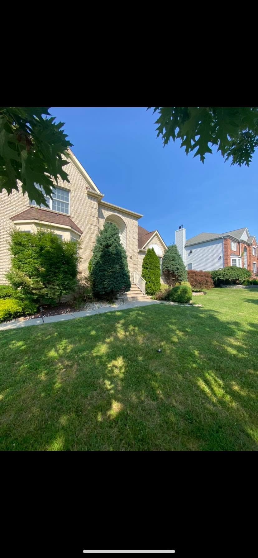 Front of a brick home with shaped evergreen shrubs and tidy planting beds by Fiorenza Landscaping